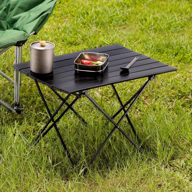 En el cesped hay una mesa plegable pequeña playa con un tupper con comida y una cuchara.